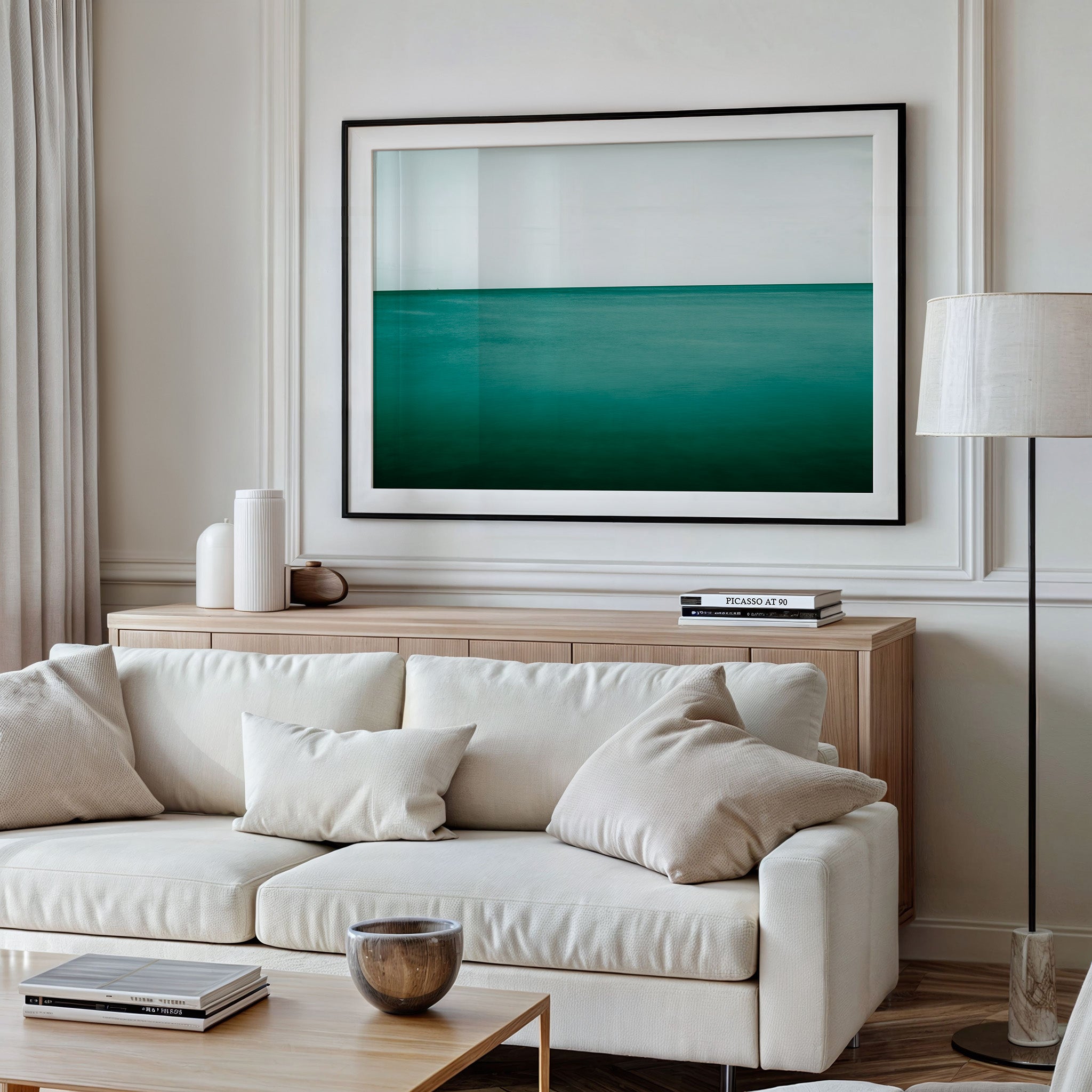 A framed photograph of a serene emerald green ocean captured at Pataua North Beach, displayed above a beige sofa in a well-lit living room setting.