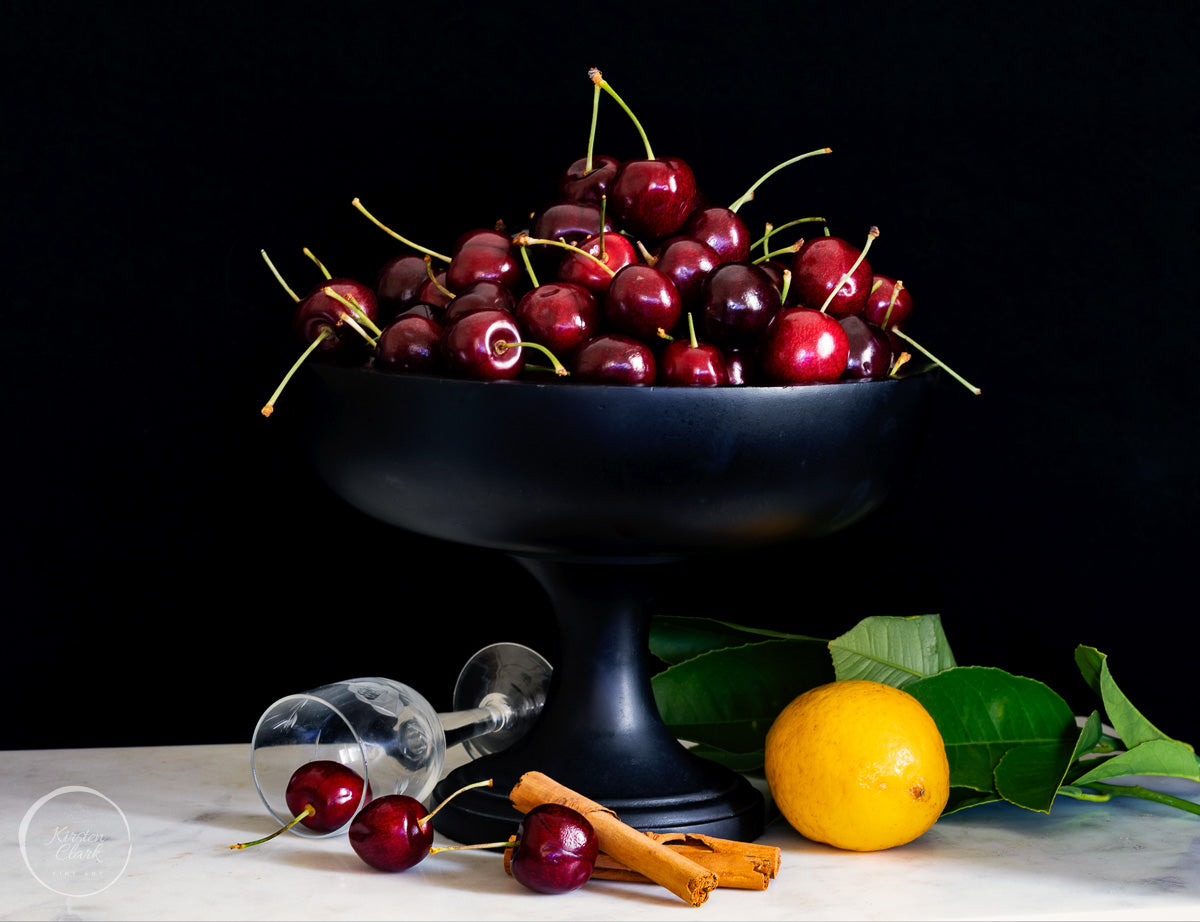 Bowl of cherries with a lemon and cinnamon sticks on a dark background
