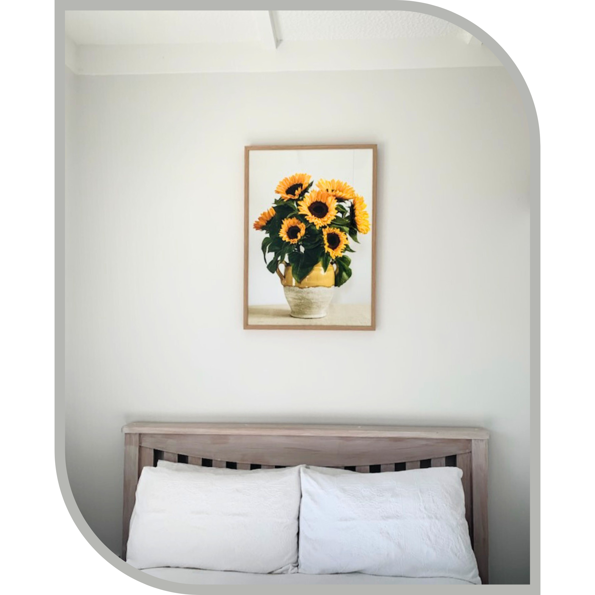 Framed artwork of sunflowers above a bed with white pillows.