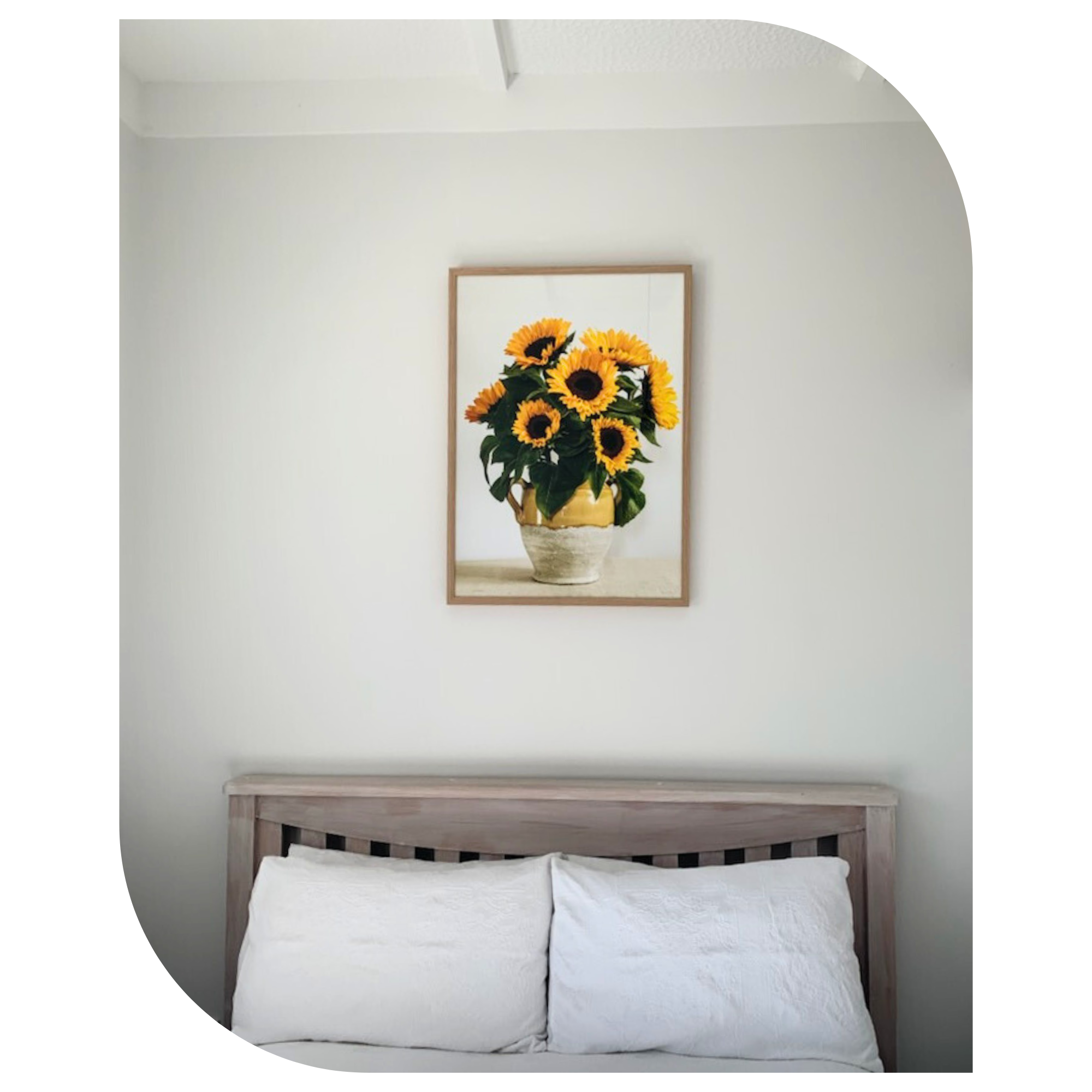 Framed artwork of sunflowers above a bed with white pillows.
